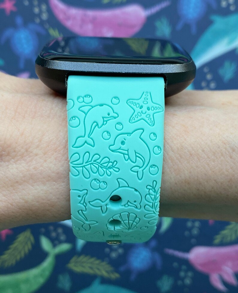 Puede incluir: Una correa de reloj de silicona azul turquesa con un dise&ntilde;o de delf&iacute;n, estrella de mar y algas marinas. La correa es compatible con un reloj inteligente.