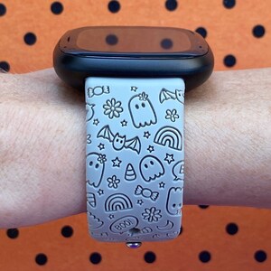 May include: A gray silicone watch band with a Halloween-themed design. The band features ghosts, bats, candy corn, stars, rainbows, and the word "BOO!" in a white outline.