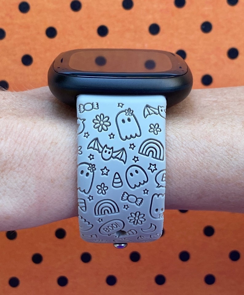 May include: A gray silicone watch band with a Halloween-themed design. The band features ghosts, bats, candy corn, stars, rainbows, and the word "BOO!" in a white outline.