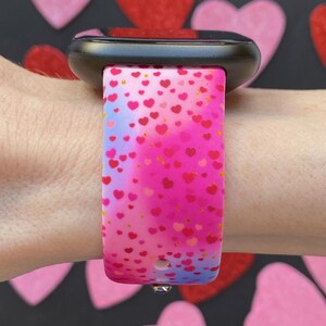 May include: A pink and blue watch band with a heart pattern. The band is made of silicone and has a black watch face.