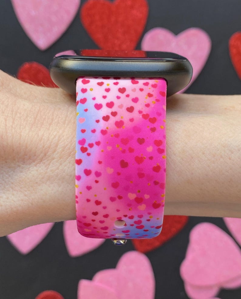 May include: A pink and blue watch band with a heart pattern. The band is made of silicone and has a black watch face.