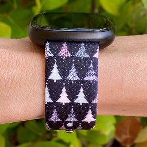 May include: A black smartwatch with a Christmas tree patterned band. The band features white, pink, and light blue trees on a black background.