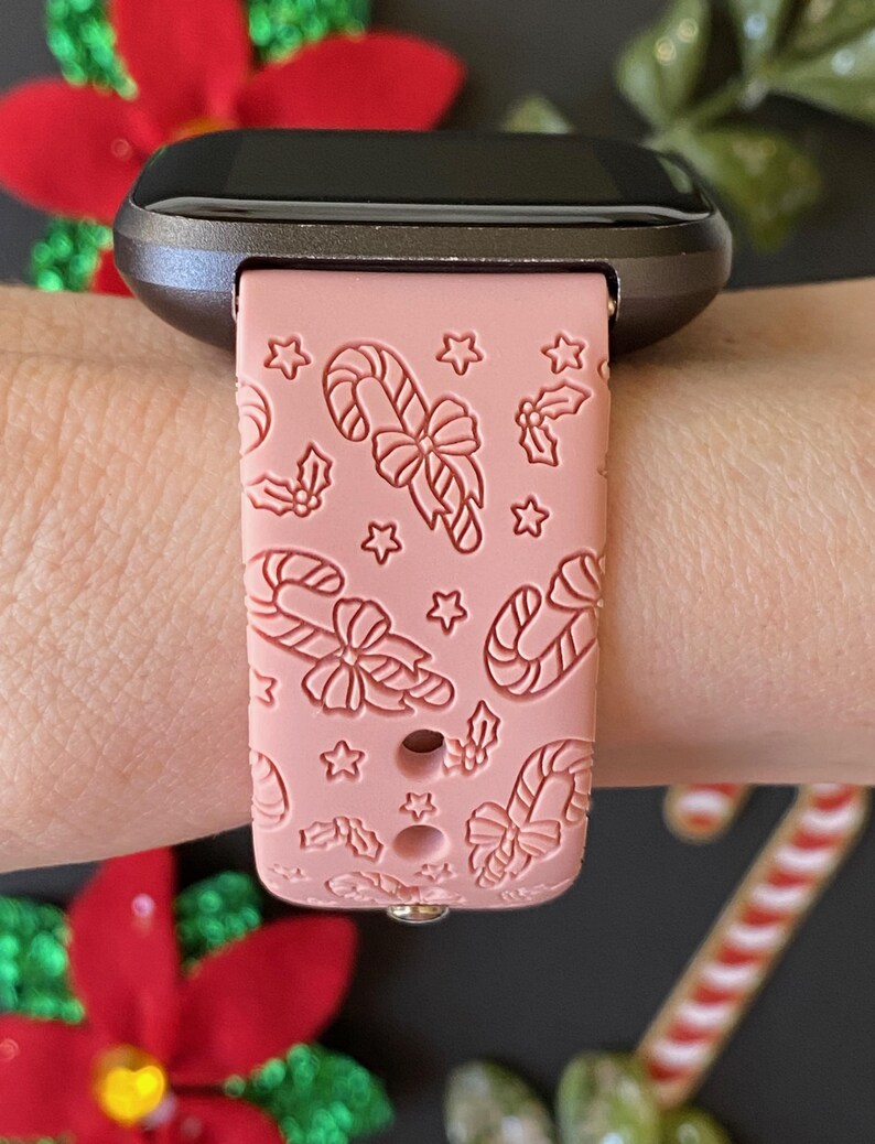 May include: A pink silicone watch band with a candy cane and holly design. The band is compatible with smartwatches.
