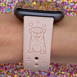 May include: A pink silicone watch band with a pug design and paw prints. The band is compatible with Fitbit watches.