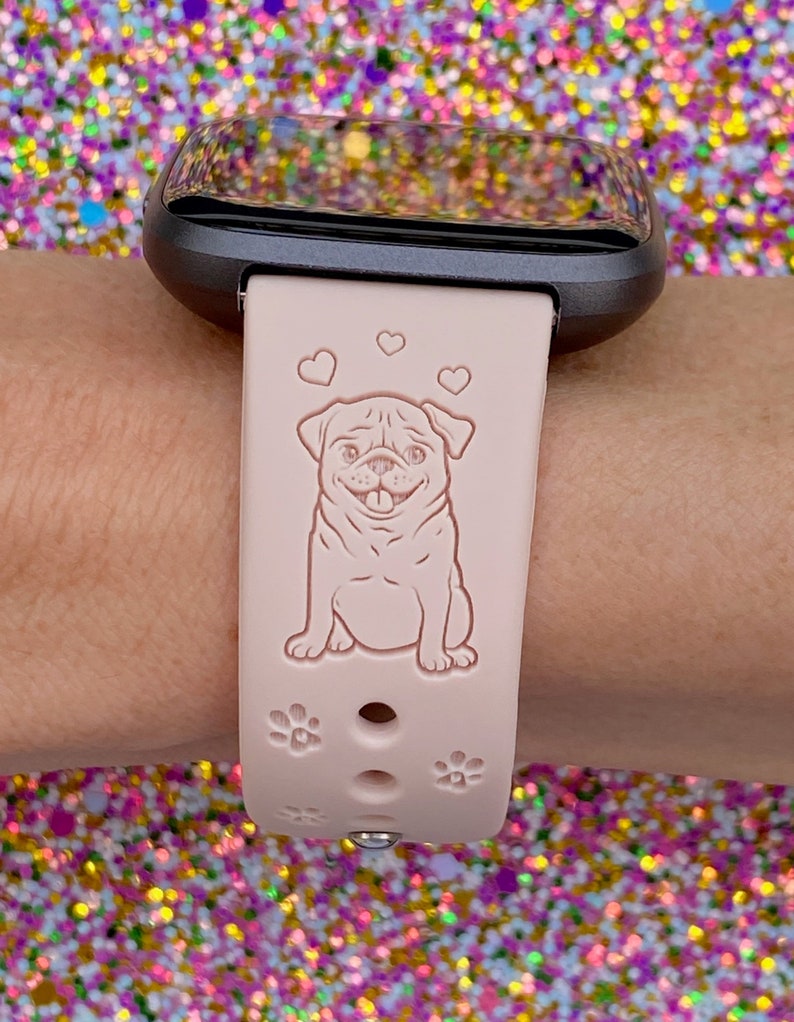 May include: A pink silicone watch band with a pug design and paw prints. The band is compatible with Fitbit watches.