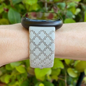 K&ouml;nnte beinhalten: Ein graues, gemustertes Silikon-Armband mit einem schwarzen Zifferblatt. Das Armband hat ein geometrisches Muster.