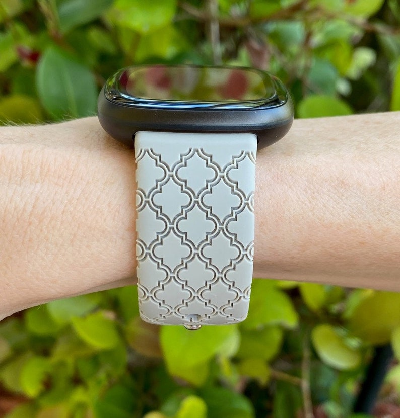 K&ouml;nnte beinhalten: Ein graues, gemustertes Silikon-Armband mit einem schwarzen Zifferblatt. Das Armband hat ein geometrisches Muster.