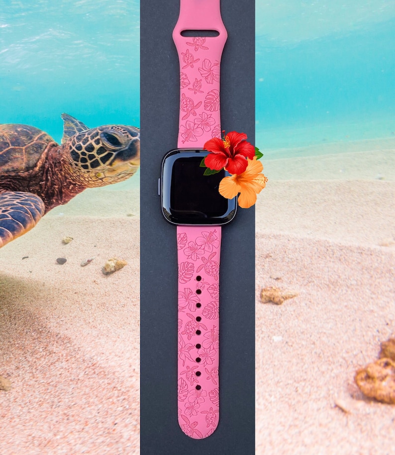 May include: Pink silicone watch band with a floral and turtle design. The band is on a black background with a flower on top of the watch face.