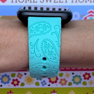 May include: A turquoise blue watch band with a paisley pattern. The band is made of silicone and has a textured surface.