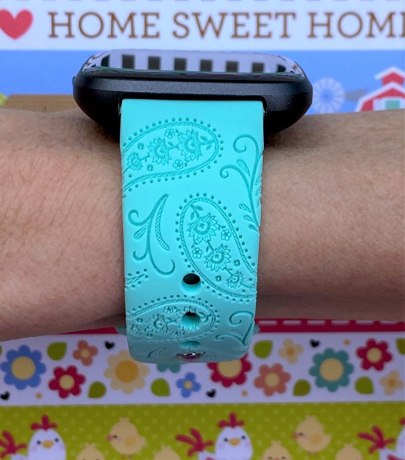 May include: A turquoise blue watch band with a paisley pattern. The band is made of silicone and has a textured surface.