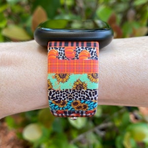 Pode incluir: Um smartwatch preto com uma banda de padr&atilde;o colorido. A banda apresenta um design multicolorido com ab&oacute;boras, girass&oacute;is, xadrez e estampa animal.
