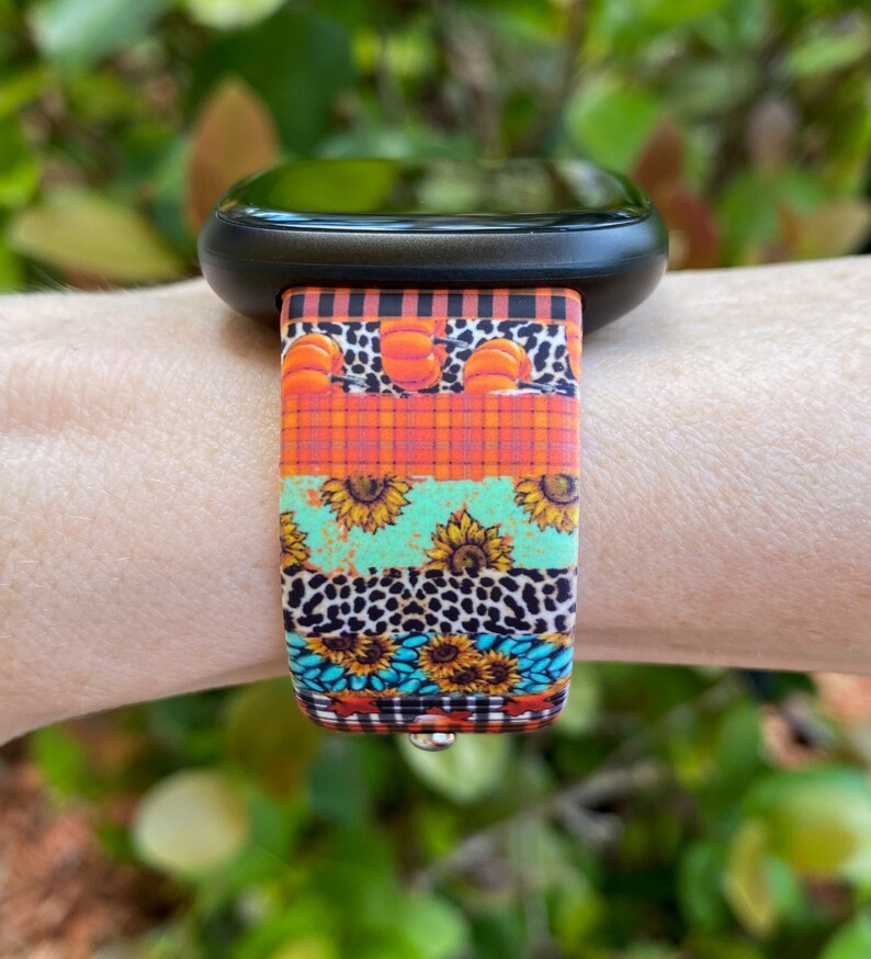Pode incluir: Um smartwatch preto com uma banda de padr&atilde;o colorido. A banda apresenta um design multicolorido com ab&oacute;boras, girass&oacute;is, xadrez e estampa animal.