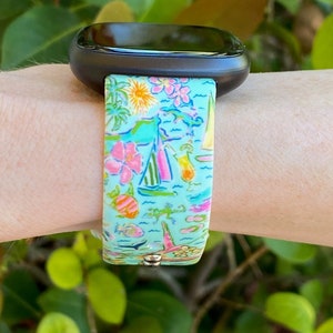 K&ouml;nnte beinhalten: Ein t&uuml;rkisfarbenes Armband mit einem bunten tropischen Muster mit Palmen, Segelbooten, Fischen und Flip-Flops. Das Armband ist aus Silikon und kompatibel mit Fitbit-Uhren.