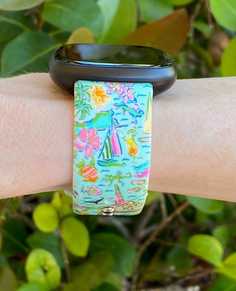 K&ouml;nnte beinhalten: Ein t&uuml;rkisfarbenes Armband mit einem bunten tropischen Muster mit Palmen, Segelbooten, Fischen und Flip-Flops. Das Armband ist aus Silikon und kompatibel mit Fitbit-Uhren.