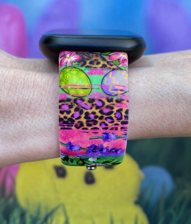 May include: A colorful watch band with a pink, green, and purple Easter egg design. The band has a leopard print pattern and lavender flowers.