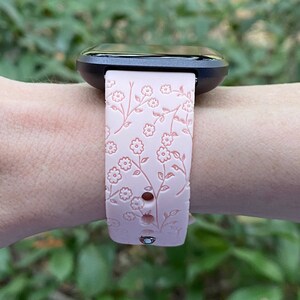 May include: A pink silicone watch band with a floral pattern. The band has a black watch face attached to it.