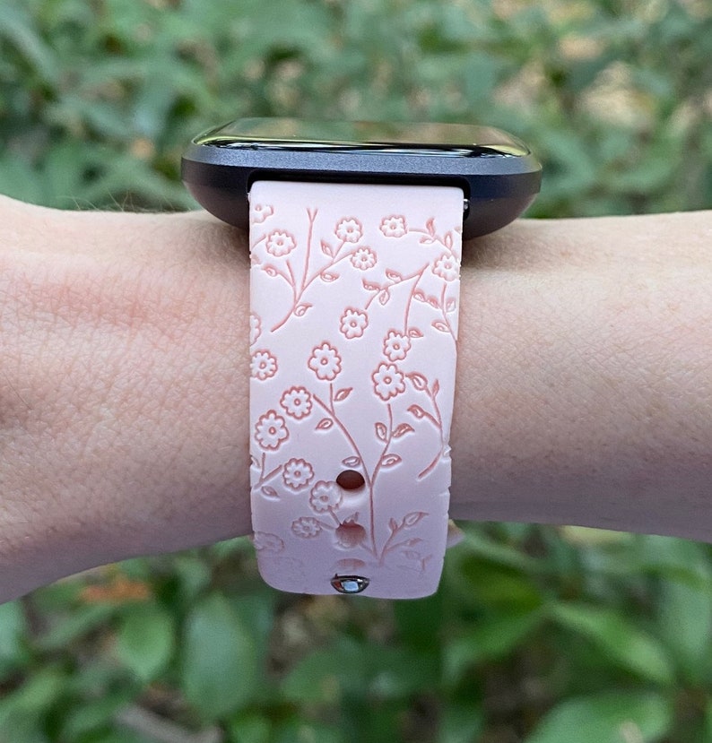 May include: A pink silicone watch band with a floral pattern. The band has a black watch face attached to it.
