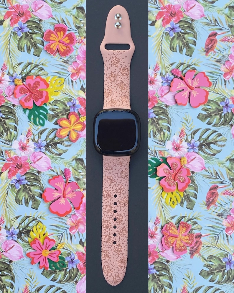 May include: A pink silicone watch band with a floral pattern. The band is designed for a smartwatch and has a black watch face.