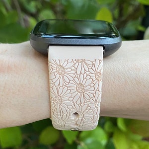 May include: A black smartwatch with a pink floral patterned silicone band. The band has a daisy design.