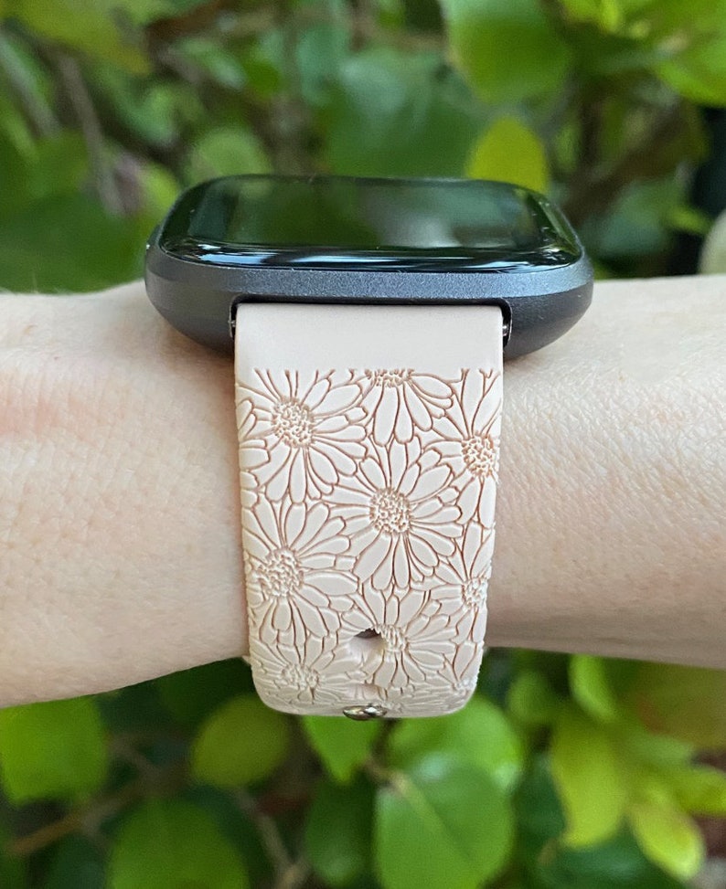 May include: A black smartwatch with a pink floral patterned silicone band. The band has a daisy design.