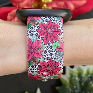 K&ouml;nnte beinhalten: Eine schwarze Apple Watch mit einem wei&szlig;en, roten und gr&uuml;nen gemusterten Armband mit Weihnachtssternen und Leopardenmuster.