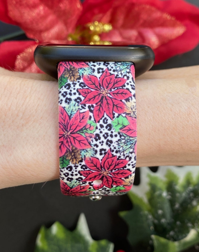 K&ouml;nnte beinhalten: Eine schwarze Apple Watch mit einem wei&szlig;en, roten und gr&uuml;nen gemusterten Armband mit Weihnachtssternen und Leopardenmuster.