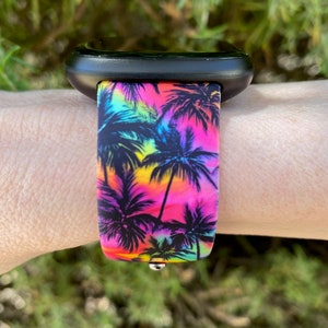 May include: A black smartwatch with a colorful palm tree print silicone band. The band features a vibrant pink, yellow, blue, and green color scheme.