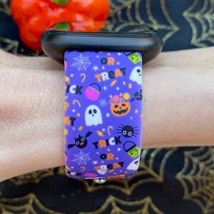 Puede incluir: Pulsera de reloj de silicona morada con tem&aacute;tica de Halloween. La pulsera presenta un patr&oacute;n repetitivo de fantasmas, murci&eacute;lagos, ara&ntilde;as, ma&iacute;z dulce y cubos de dulces con el texto "Trick or Treat".