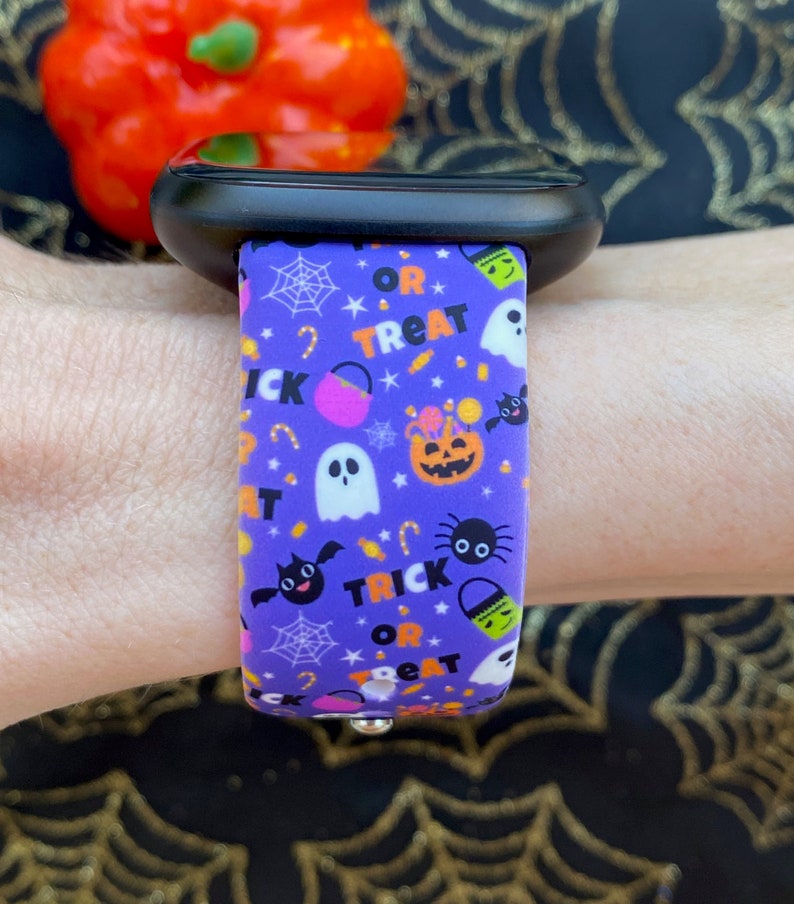 Puede incluir: Pulsera de reloj de silicona morada con tem&aacute;tica de Halloween. La pulsera presenta un patr&oacute;n repetitivo de fantasmas, murci&eacute;lagos, ara&ntilde;as, ma&iacute;z dulce y cubos de dulces con el texto "Trick or Treat".