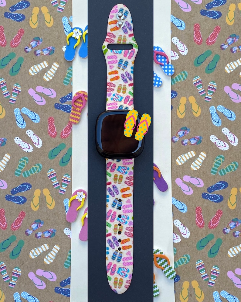 May include: A white Apple Watch band with a colorful flip-flop pattern. The band is made of silicone and has a black watch face.