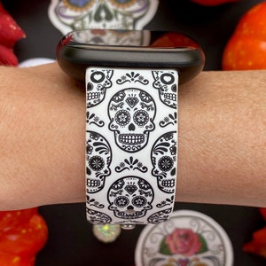 May include: White and black watch band with a repeating pattern of sugar skulls. The band is made of silicone and has a smooth finish.
