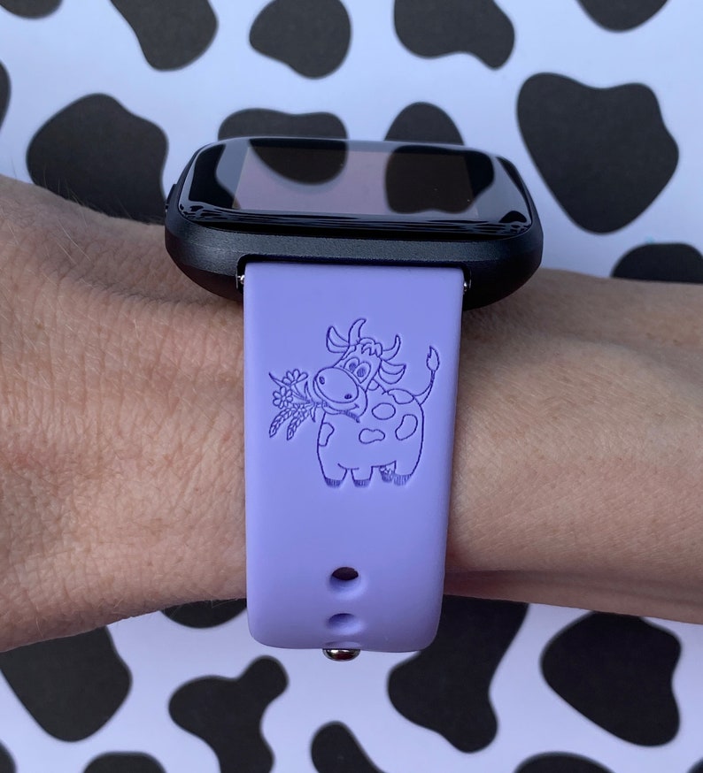 Peut inclure: Un bracelet de montre en silicone violet avec un cadran noir. Le bracelet est d&eacute;cor&eacute; d'un motif de vache de dessin anim&eacute; avec une fleur dans sa bouche.