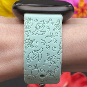 May include: A light blue silicone watch band with a sea life design. The band features sea turtles, starfish, crabs, and coral.