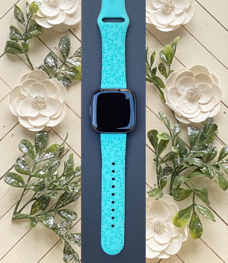 May include: A turquoise blue Apple Watch band with a floral pattern. The band is made of silicone and has a smooth finish.