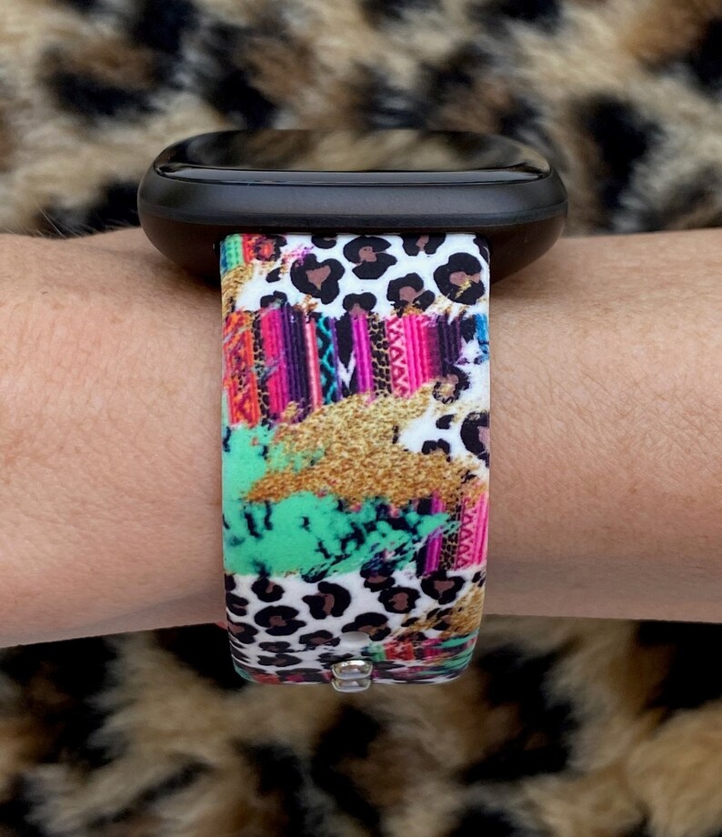 May include: A colorful watch band with a leopard print, pink, green, and gold accents. The band is made of silicone and has a white background.