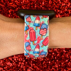 May include: A black Apple Watch band with a blue, white, and red popsicle pattern. The popsicles are decorated with stars and stripes.
