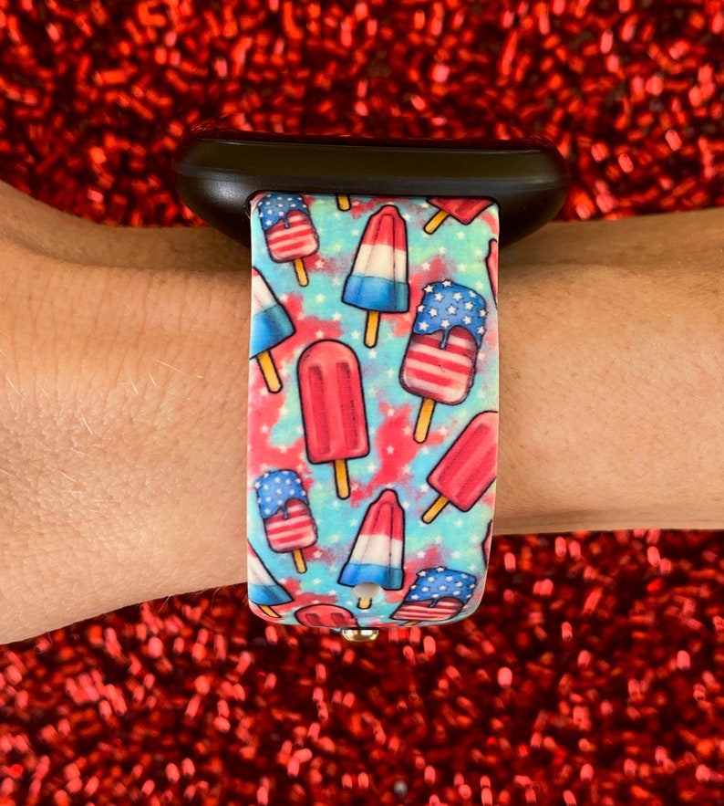 May include: A black Apple Watch band with a blue, white, and red popsicle pattern. The popsicles are decorated with stars and stripes.
