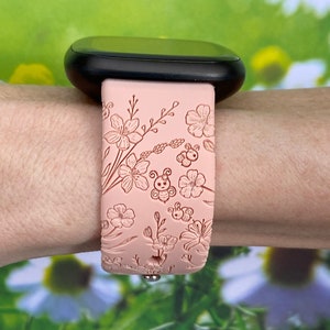 May include: A pink silicone watch band with a floral and bee design. The band is embossed with a delicate pattern of flowers and bees.