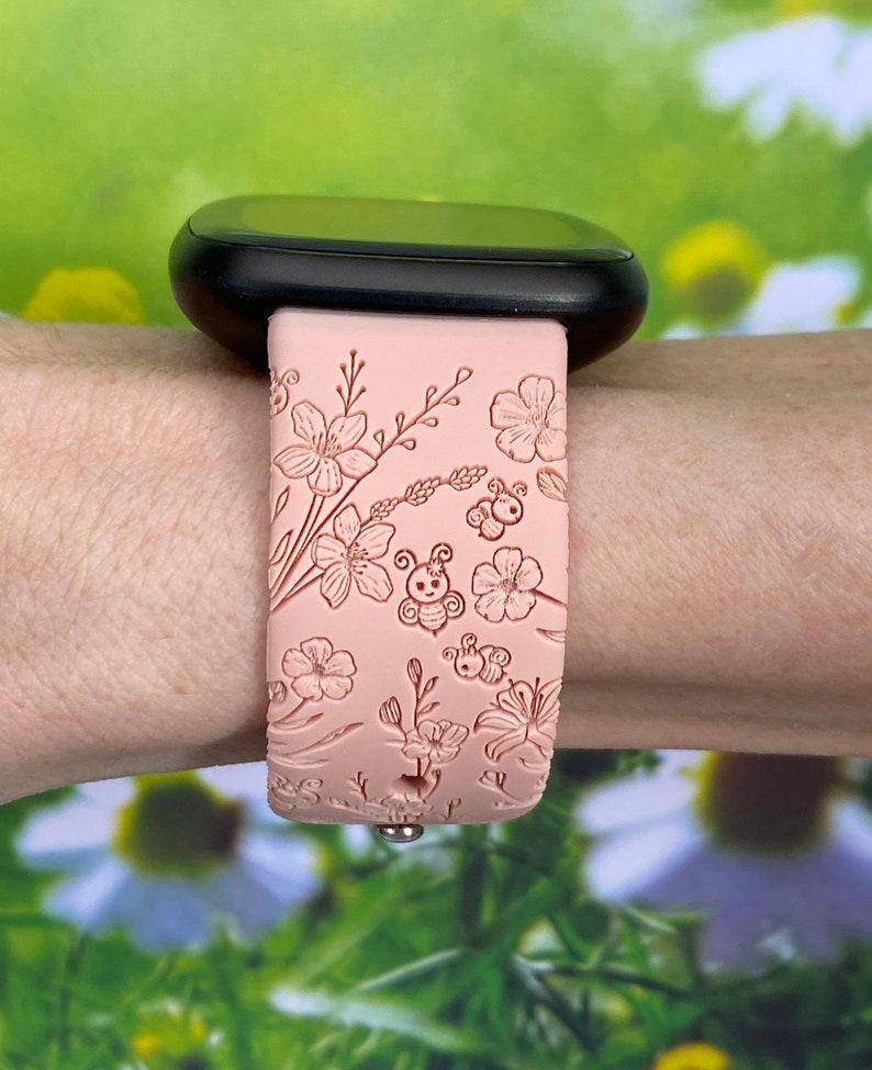 May include: A pink silicone watch band with a floral and bee design. The band is embossed with a delicate pattern of flowers and bees.