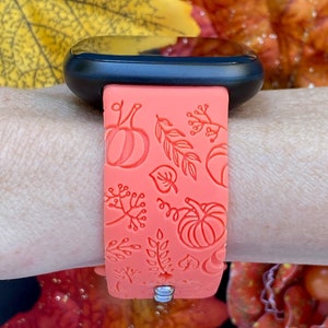 May include: A coral pink silicone watch band with a fall-themed design featuring pumpkins and leaves.
