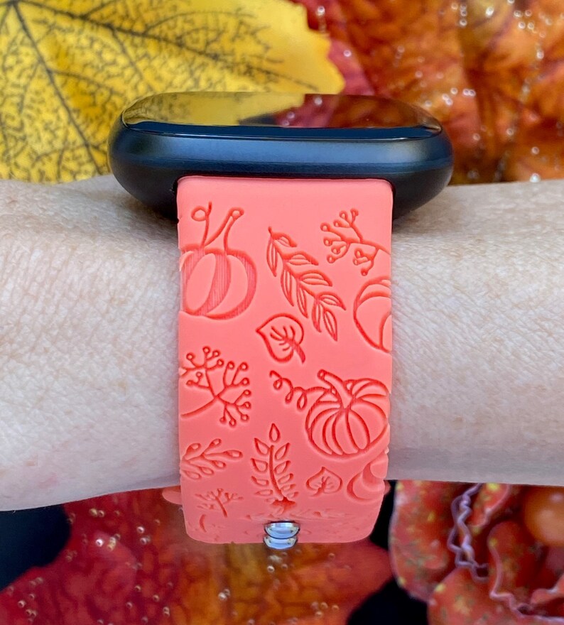 May include: A coral pink silicone watch band with a fall-themed design featuring pumpkins and leaves.