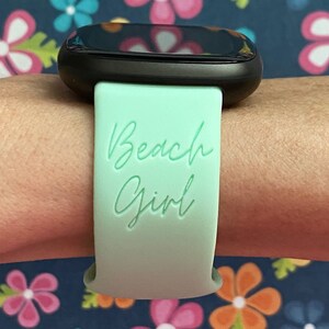 May include: A mint green smartwatch band with the text "Beach Girl" printed on it.