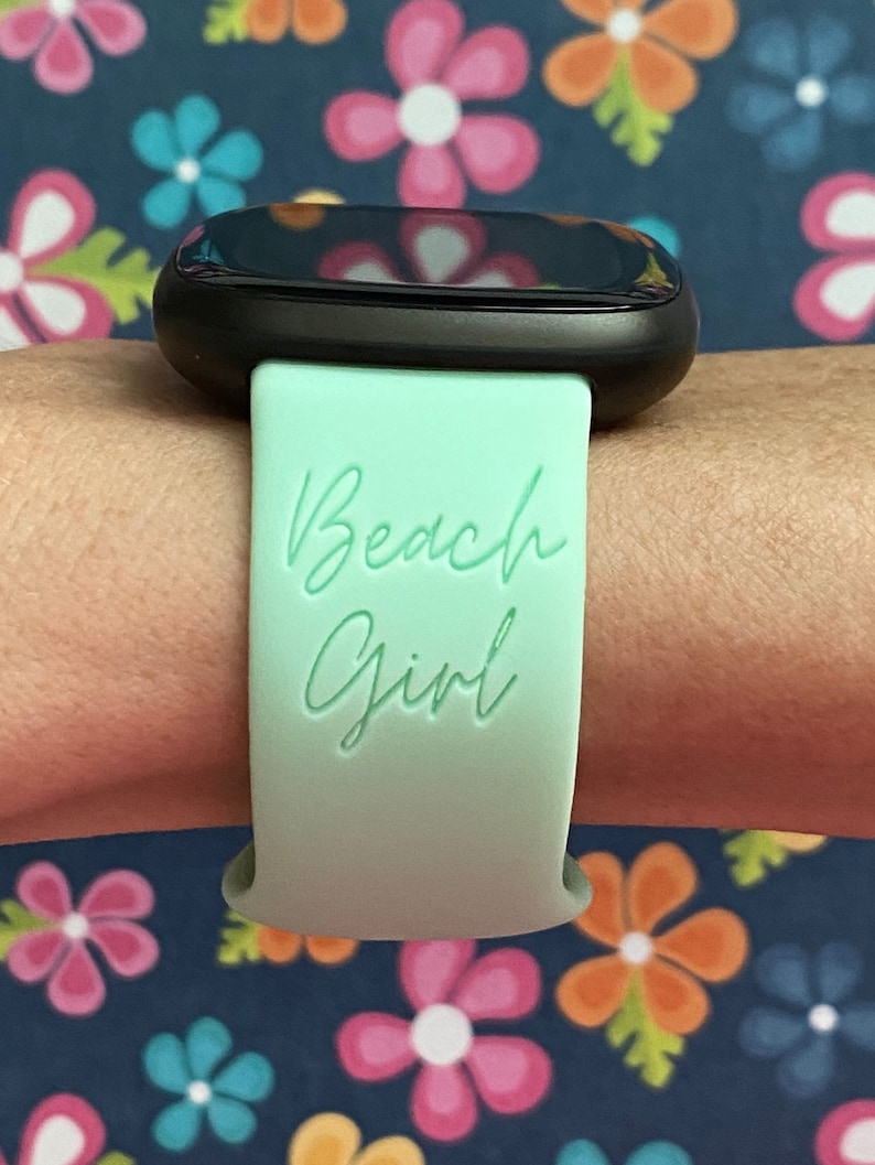 May include: A mint green smartwatch band with the text "Beach Girl" printed on it.