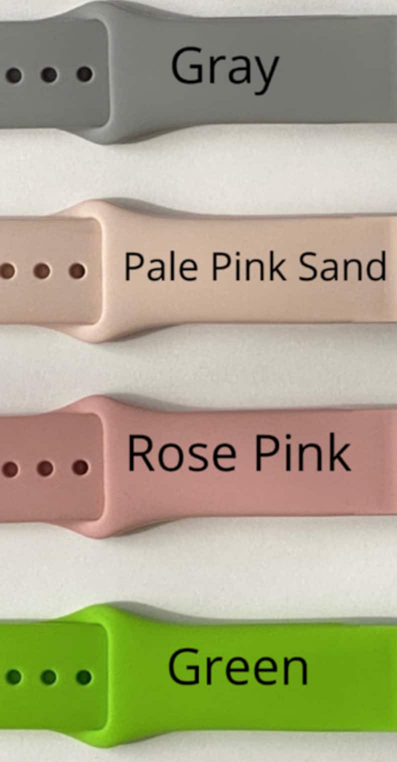 May include: A close-up of four watch bands in different colors: gray, pale pink sand, rose pink, and green. Each band has the color name printed in black. The bands are made of a flexible material and have holes for adjustment.