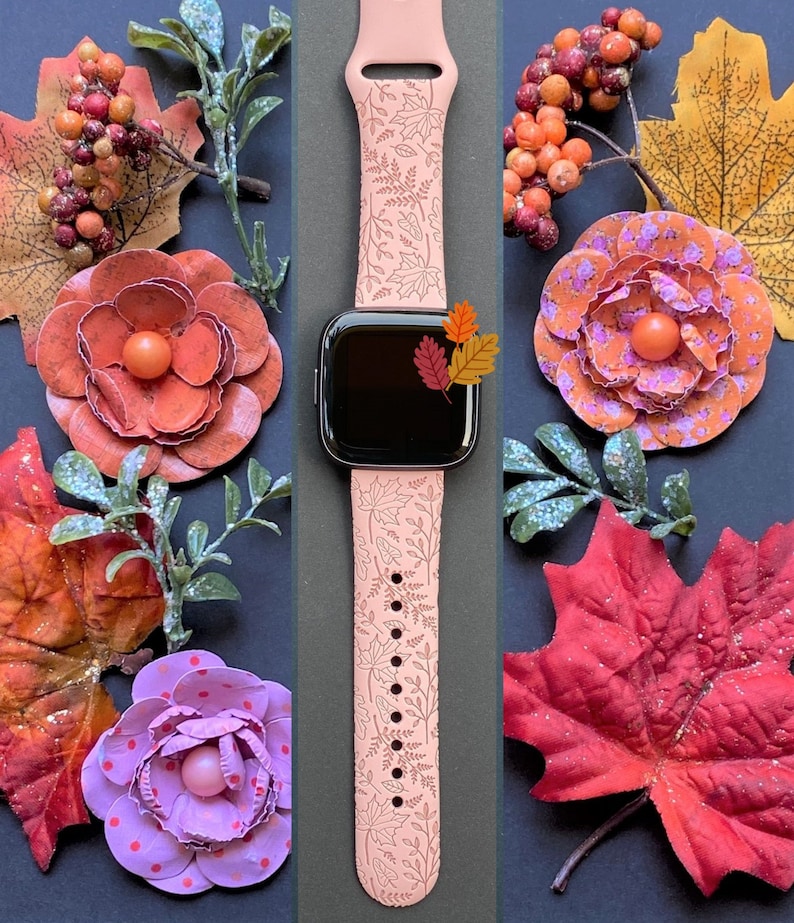 May include: A pink watch band with a fall leaf pattern. The band is made of silicone and has a white outline of the leaves. The band is shown on a black background with fall-themed decorations.
