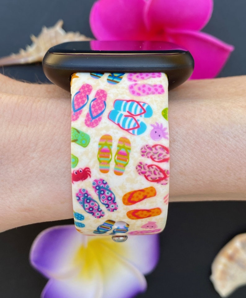 May include: A white watch band with a colorful print of flip flops, crabs, and seashells. The band is made of silicone and is compatible with Apple Watch.