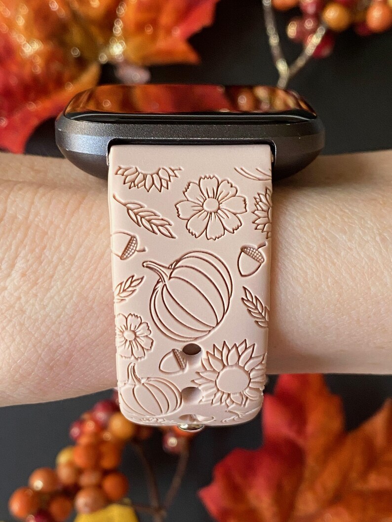 May include: A blush pink silicone watch band with a fall-themed design. The band features pumpkins, sunflowers, acorns, and wheat stalks.