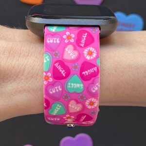 Puede incluir: Banda de reloj rosa con un patr&oacute;n de corazones de caramelo. Los corazones tienen las palabras "cute", "sweet", "love" y "angel" en ellos.
