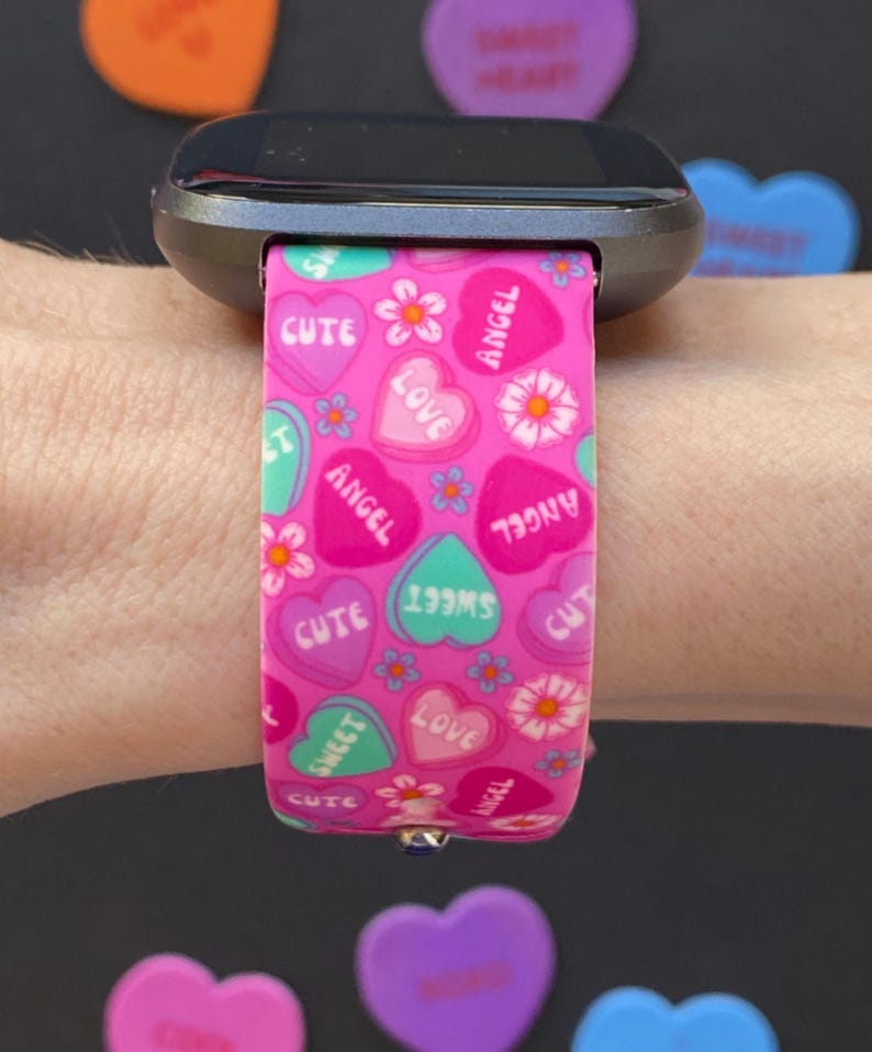 Puede incluir: Banda de reloj rosa con un patr&oacute;n de corazones de caramelo. Los corazones tienen las palabras "cute", "sweet", "love" y "angel" en ellos.