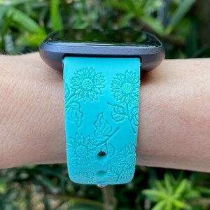 May include: A turquoise blue watch band with a sunflower pattern. The band is made of silicone and has a textured surface.